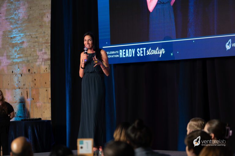 A woman in a long dark dress speaks on stage at a 