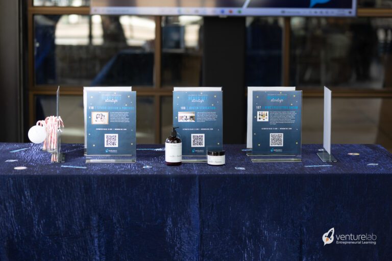 A table displays several informational stands, bottles, and a container with candy canes. The tablecloth is blue and has a 