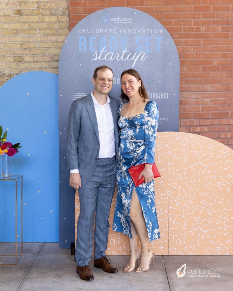 A man and woman dressed formally pose in front of a colorful backdrop with 