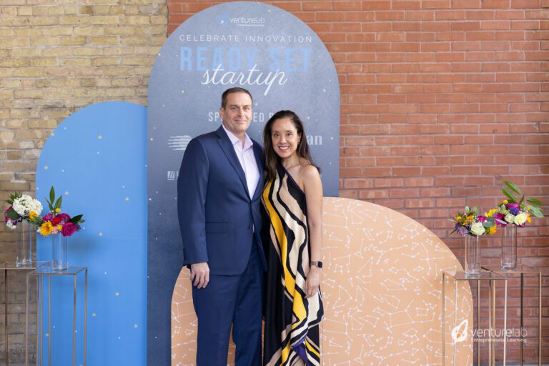 A man and woman in formal attire stand in front of a 