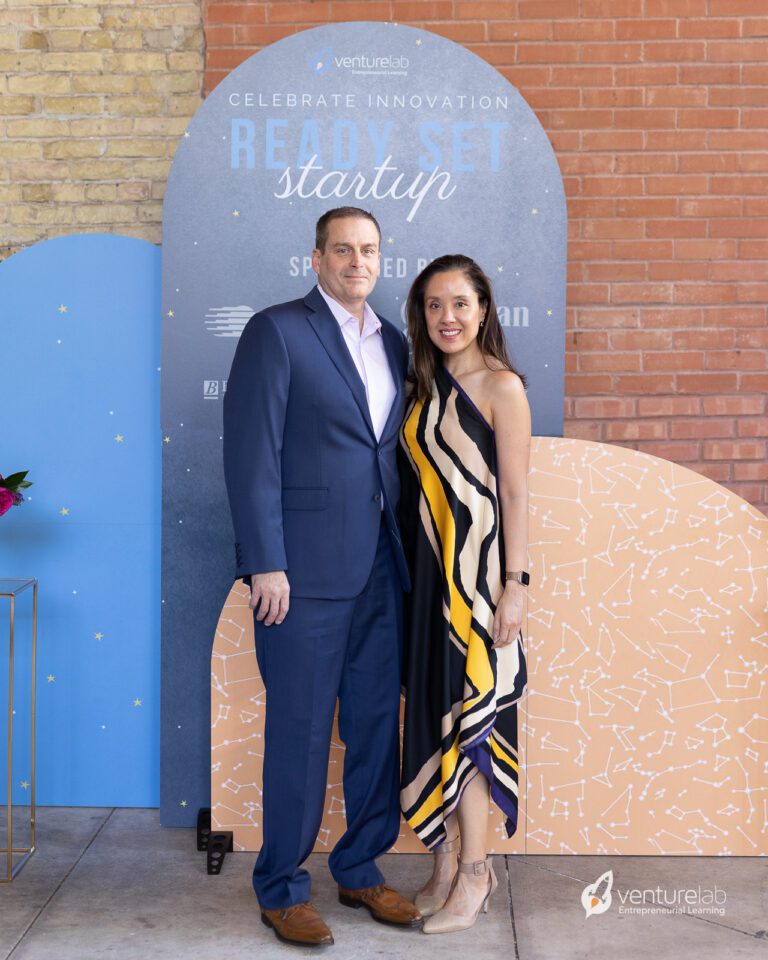 A man and a woman standing together at the Ready Set Startup Gala, posing in front of a promotional backdrop.