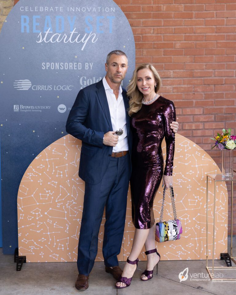 A man and woman pose together at an event in front of a sign reading 