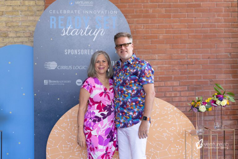 Two individuals stand side by side in front of a 
