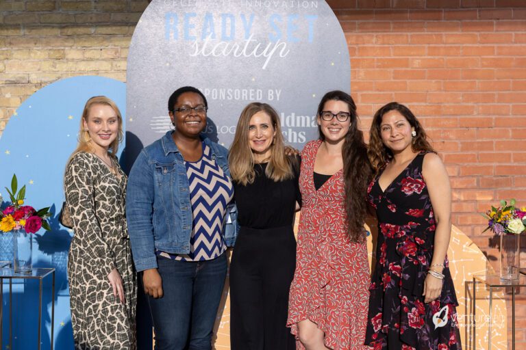 Five women pose together in front of a 
