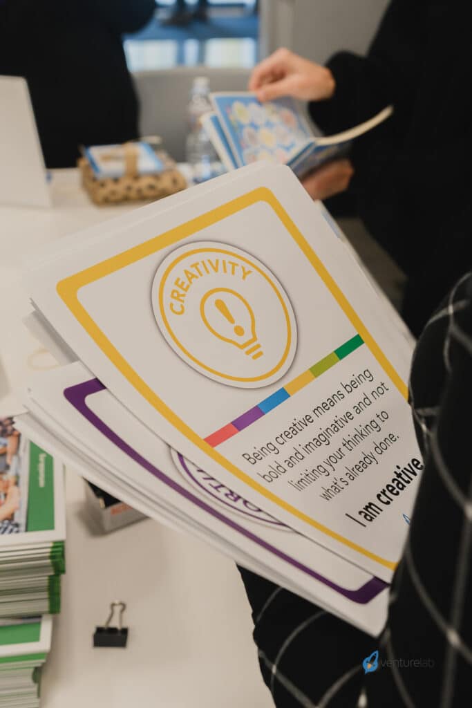 A person holds a card labeled "Creativity" that reads, "Being creative means being bold and imaginative and not limiting your thinking to what’s already been," highlighting the essence of youth entrepreneurship education.
