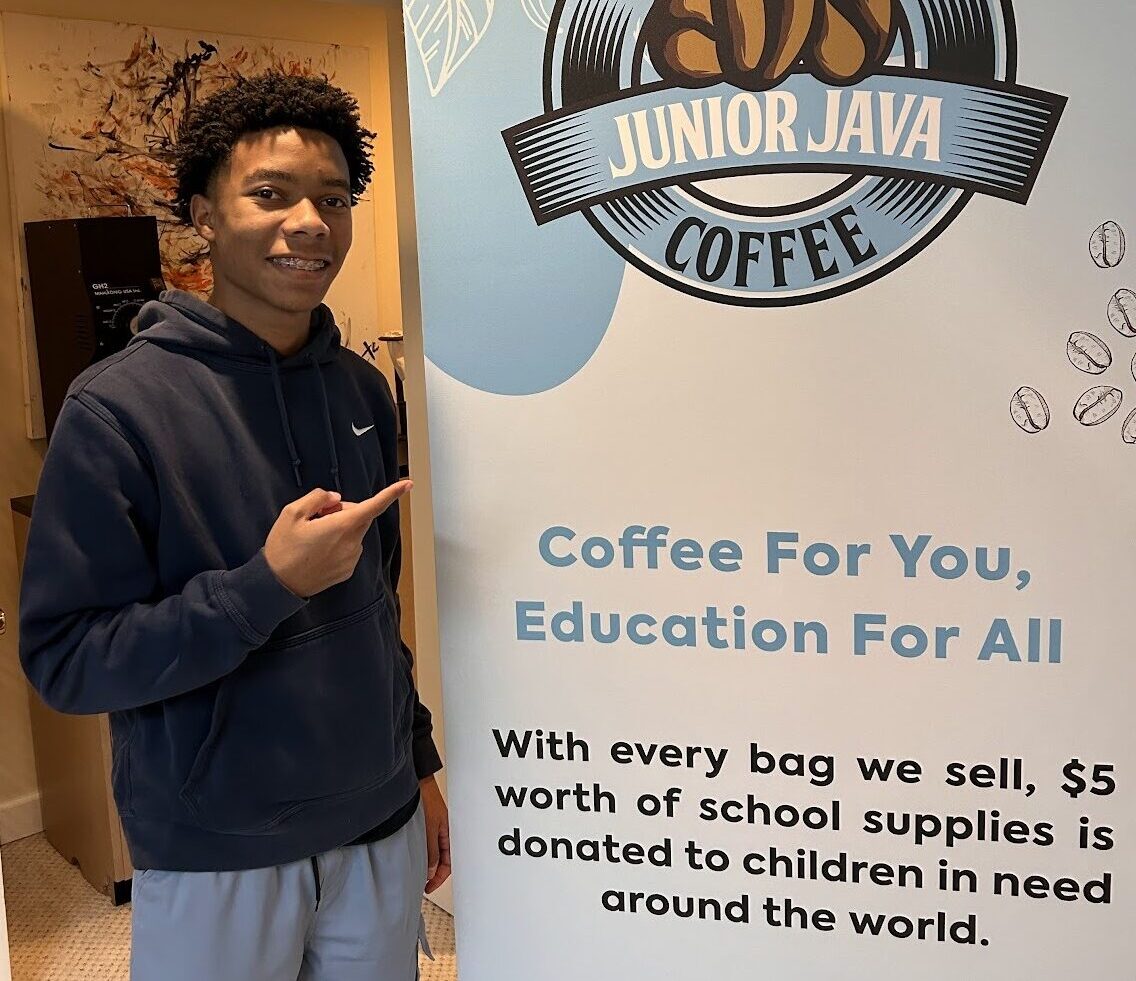 A young man standing next to a banner that says coffee for education for all, showcasing VentureLab's impact.