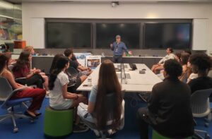 A man standing in front of a group of people sitting around a table at the VentureLab and Saint Louis University partnership meeting.