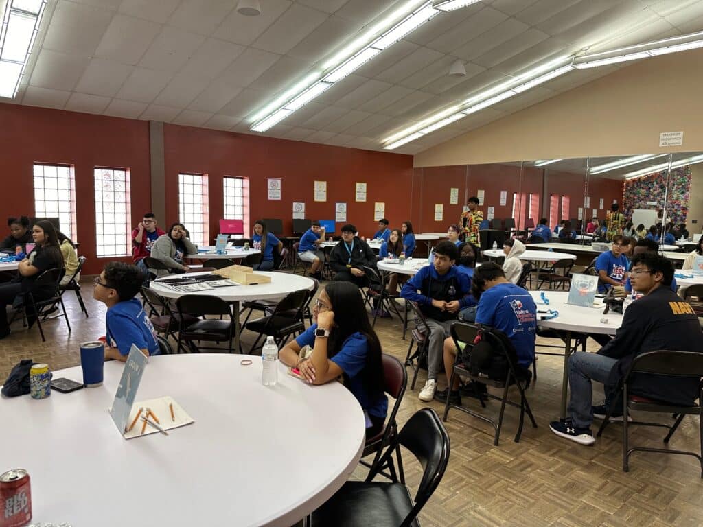 A group of people seated at round tables in a community room, listening attentively to the VentureLab Idea to Pitch program implementation strategies.