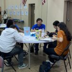 In a room adorned with American flags and posters, people gather around a table with snacks and a sign labeled "Group 6" during the student pitch event at the Garcia Center.