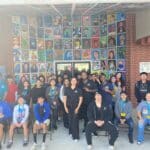 A group of people, including students and staff, posing in front of a wall covered with colorful artwork, showcases the enthusiasm from the Garcia Center Spring Break Camp Youth Entrepreneurship program.