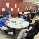 A group of people sit around a table at the Garcia Center, engaged in a lively discussion for the Idea to Pitch event. Computers are in the background, capturing the energy and focus in this classroom setting.