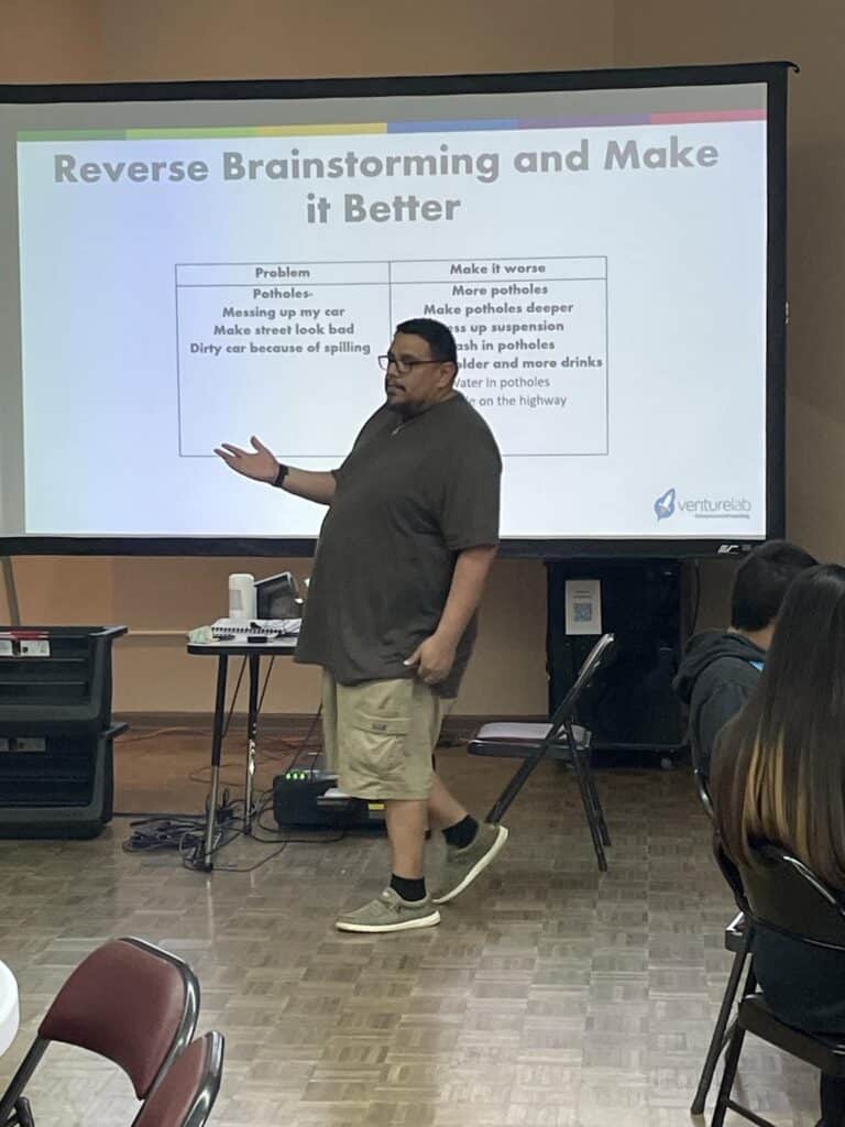 At the Garcia Center Spring Break Camp, a person presents a slide titled "Reverse Brainstorming and Make it Better," highlighting a list of problems and innovative solutions. This engaging session is part of the Youth Entrepreneurship program, designed to inspire young minds.