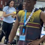 In a vibrant room, two people engage in animated discussions. One sports a colorful shirt and lanyard brimming with badges, while the other clutches a yellow item. The space, adorned with tables and decorations, buzzes with energy—ideal for exchanging ideas to pitch and fostering near-peer mentoring.