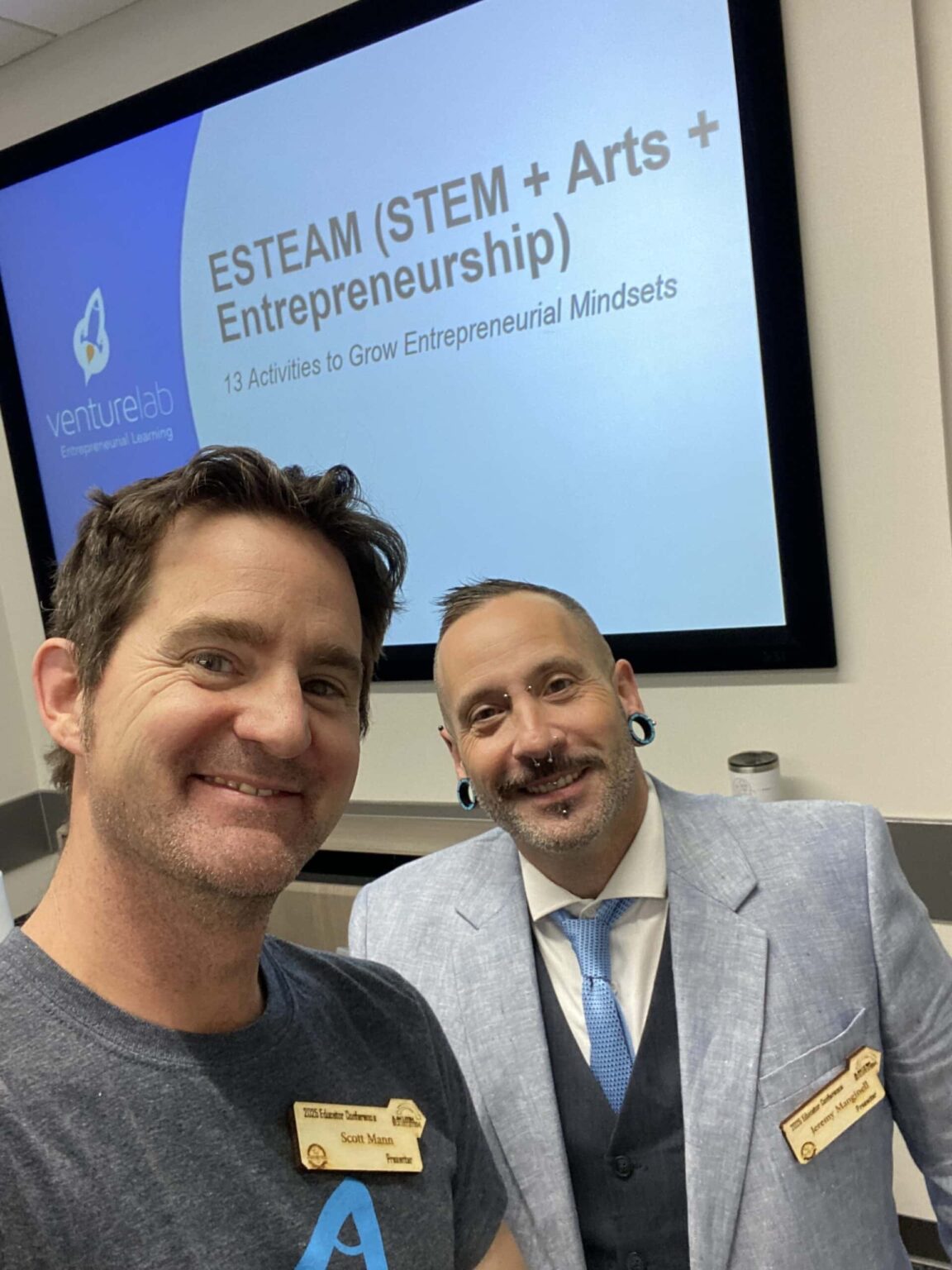 Two people smiling in front of a presentation titled "ESTEAM (STEM + Arts + Entrepreneurship)" with a subheading about activities to grow entrepreneurial mindsets.