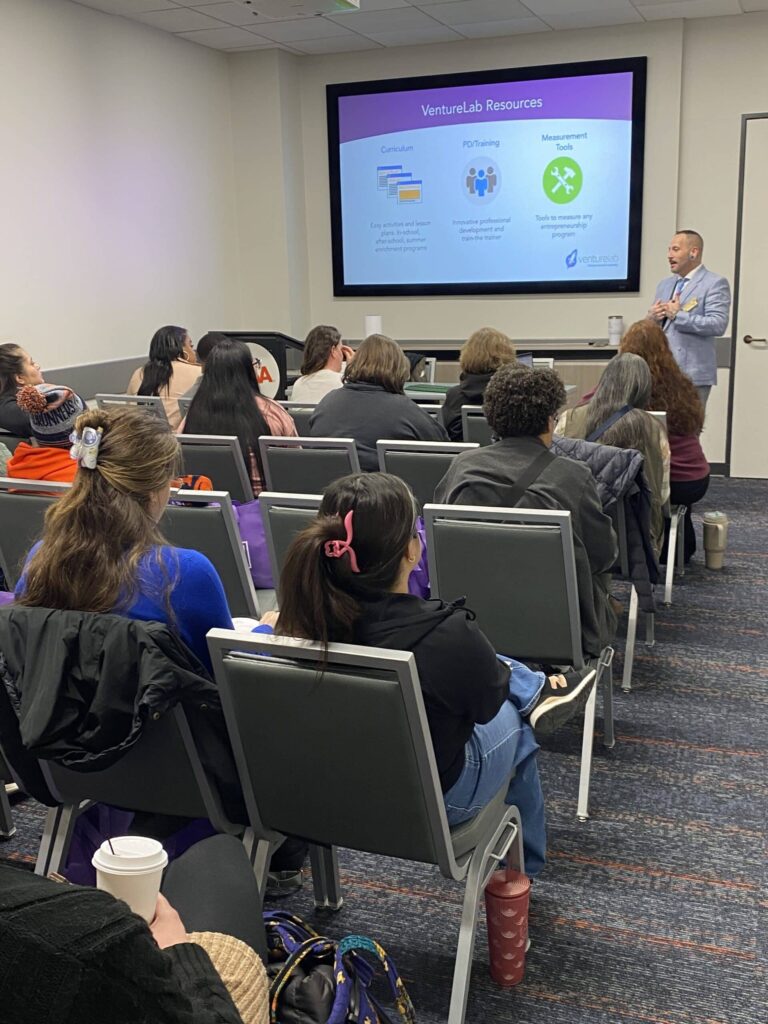 A person presents a slideshow titled "VentureLab Resources" to an audience seated in a classroom setting.