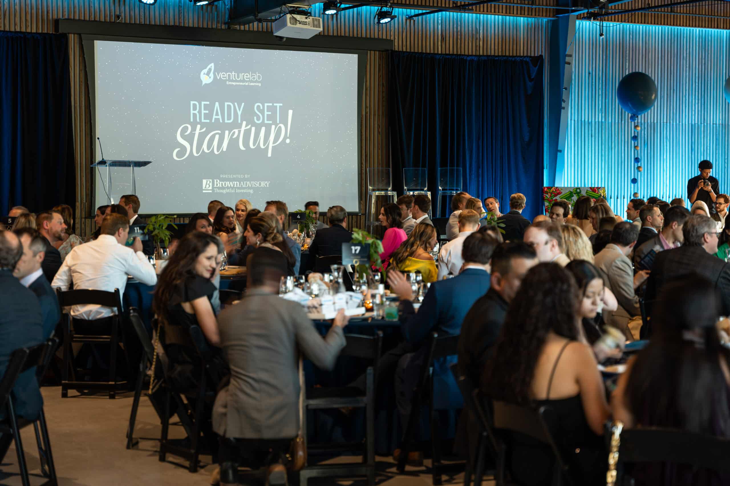 Group of attendees eating dinner and watching presentation for Ready, Set, Startup! 2025