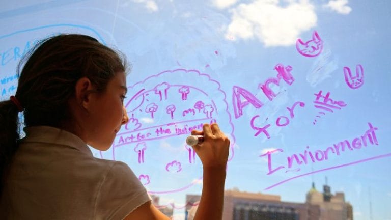 A young girl showing divergent thinking skills by brainstorming ideas with an expo marker on a window overlooking a city scene
